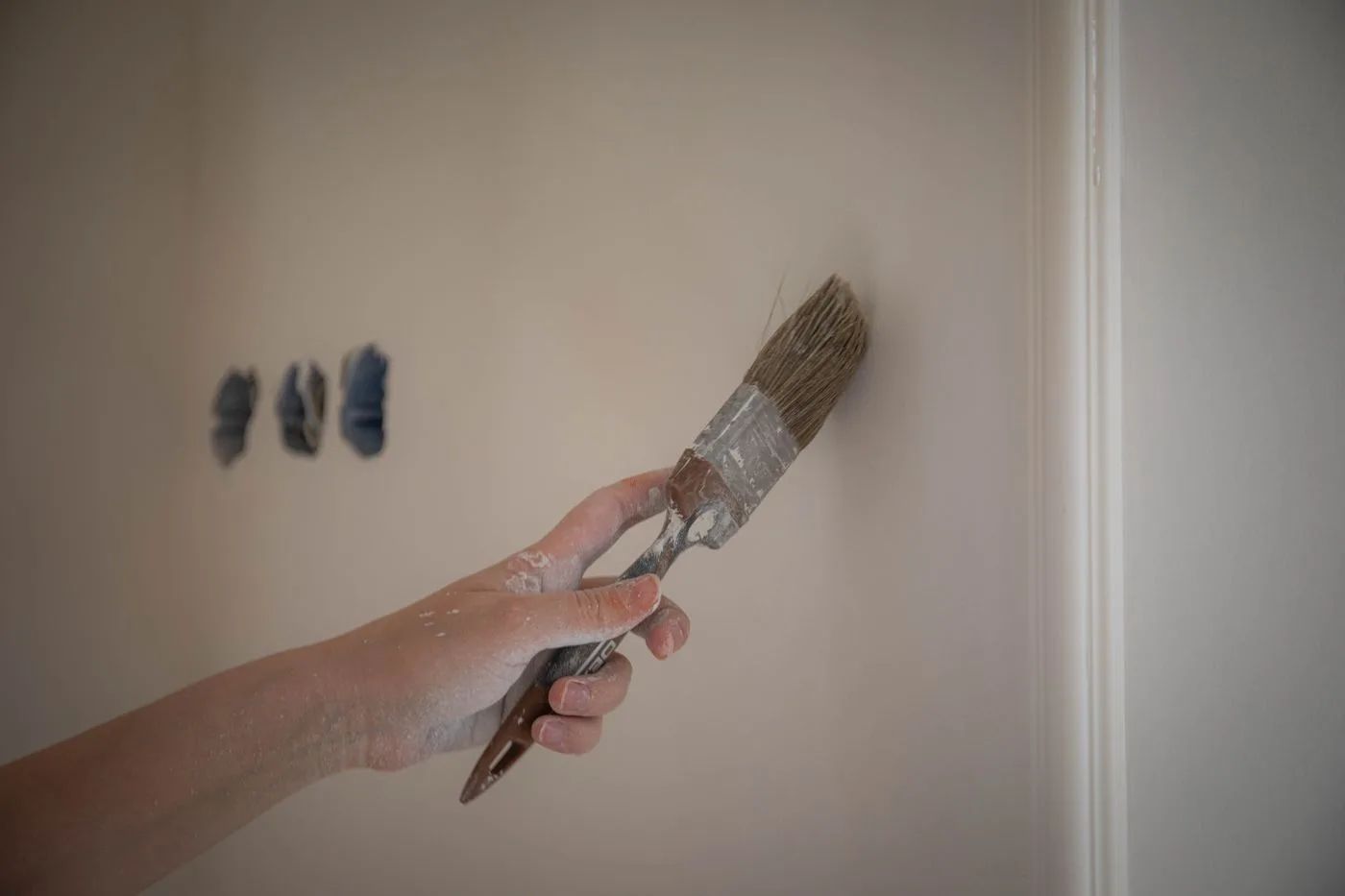 Mano aplicando pintura con una brocha junto al marco de una puerta